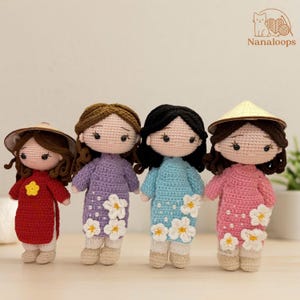 May include: Four handmade crochet dolls. Each doll wears a different coloured dress: red, purple, blue, and pink. The dresses are decorated with white flower accents and pearl-like beads. Two dolls wear conical hats. The dolls have black eyes and brown or black hair.