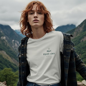 May include: White crew neck t-shirt with Korean text and a small heart graphic. The text reads "Dear My Sunshine". The model is wearing a plaid jacket and blue jeans, with a mountain backdrop.