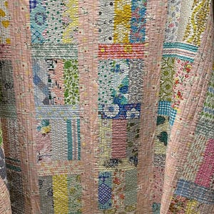May include: A patchwork quilt with a pink background and various colorful squares with different patterns. The quilt is made of cotton fabric and has a quilted texture.