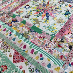 May include: A colorful patchwork quilt with the name "Priscilla" at the top. The quilt features a central floral design and is composed of various fabric patterns, including floral, striped, and geometric designs. The quilt is signed "Margaret Sampson George" with the text "Take an Element".