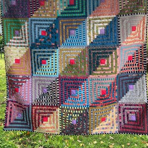 Pode incluir: Um cobertor colorido feito de quadrados com um padrão de cabana de madeira. O cobertor é feito de vários tecidos com padrões e cores diferentes, incluindo vermelho, azul, verde, amarelo e preto.