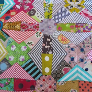 May include: A colourful patchwork quilt featuring a range of fabrics and patterns, including stripes, polka dots, and floral designs. The quilt is made up of squares and diamonds, and the colours are bright and cheerful.