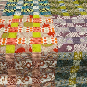 May include: A patchwork quilt featuring a grid of squares in various patterns and colors, including bright orange, lime green, purple, and blue. The fabric blocks display floral, geometric, and polka dot prints stitched together in a repeating pattern.