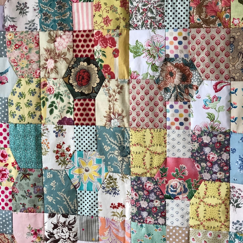 K&ouml;nnte beinhalten: Ein Patchwork-Deckenst&uuml;ck mit verschiedenen Blumenmustern in Rosa-, Rot-, Gelb-, Blau- und Gr&uuml;nt&ouml;nen. Die Decke besteht aus Quadraten und Sechsecken und der Stoff ist eine Mischung aus bedruckten und einfarbigen Stoffen.