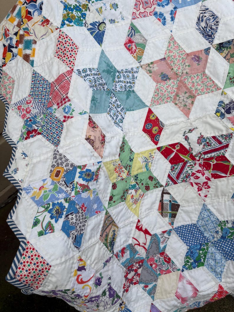 May include: A handmade quilt with a star pattern. The quilt features a variety of colorful floral and geometric patterned fabrics, including red, blue, and yellow, set against white fabric. The quilt is edged with a striped fabric.