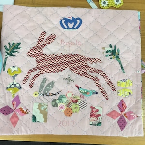 May include: A pink quilted fabric square with a red and white patterned bunny, a blue crown, and the text "Projects 2017".