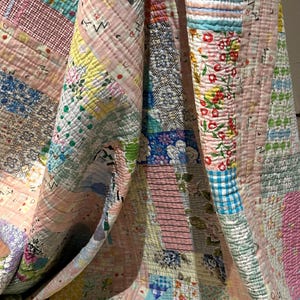 Puede incluir: Una colcha de retazos hecha con diferentes telas con estampados florales y geom&eacute;tricos en tonos rosa, azul, amarillo y verde. La colcha est&aacute; doblada por la mitad, revelando las intrincadas costuras y los diferentes patrones de las telas.