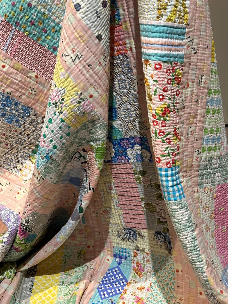 Puede incluir: Una colcha de retazos hecha con diferentes telas con estampados florales y geom&eacute;tricos en tonos rosa, azul, amarillo y verde. La colcha est&aacute; doblada por la mitad, revelando las intrincadas costuras y los diferentes patrones de las telas.