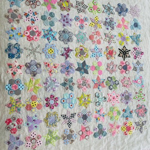 May include: A quilt made of various fabric scraps in shades of pink, blue, green, yellow, and white. The quilt is made up of a repeating pattern of stars and hexagons.