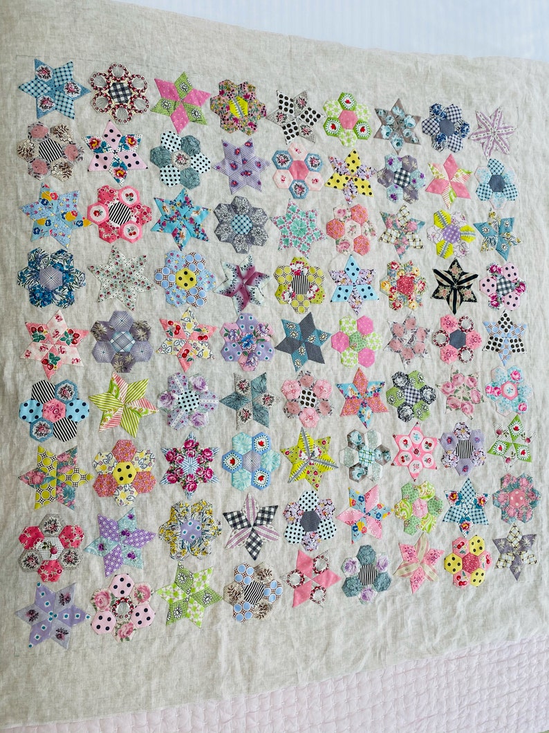 May include: A quilt made of various fabric scraps in shades of pink, blue, green, yellow, and white. The quilt is made up of a repeating pattern of stars and hexagons.