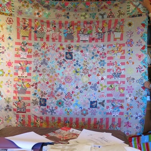 May include: A large, colorful quilt with a patchwork design featuring various floral patterns, geometric shapes, and a striped border. The quilt is displayed on a bed with other fabric scraps and sewing supplies.