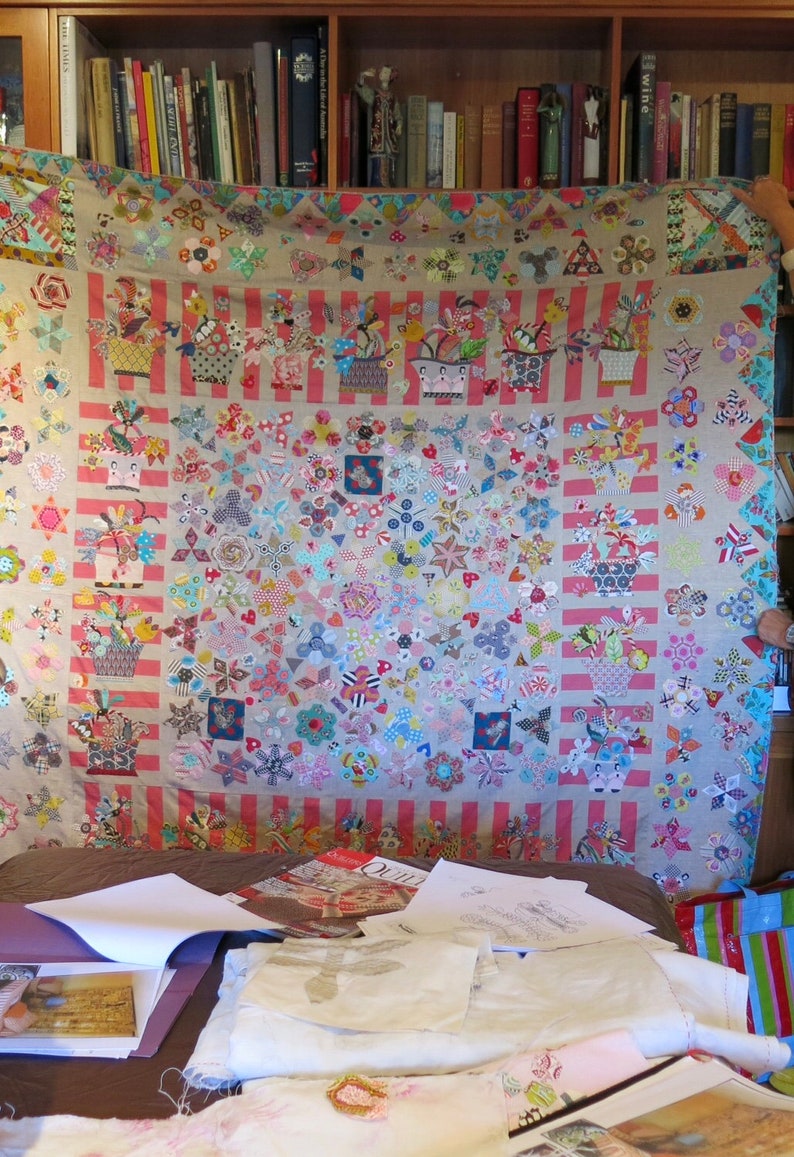 May include: A large, colorful quilt with a patchwork design featuring various floral patterns, geometric shapes, and a striped border. The quilt is displayed on a bed with other fabric scraps and sewing supplies.