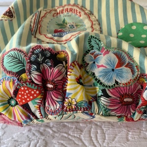May include: A yellow and blue striped fabric bag with a variety of colorful floral and polka dot patches. The bag has a label that reads "Cherries Fruit Fresh From".