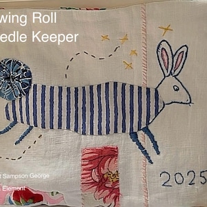 May include: A handmade sewing roll needle keeper with a whimsical design. The cream-colored fabric features an embroidered rabbit with blue and white striped body. The text "Sewing Roll Needle Keeper" and the year "2025" are also visible.
