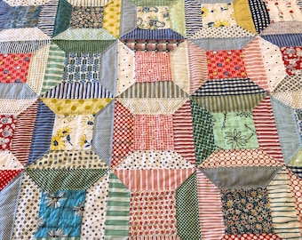 Könnte beinhalten: Eine Decke aus verschiedenen bunten Stoffen mit einem geometrischen Muster. Die Decke besteht aus Quadraten und Rechtecken in Rot-, Blau-, Grün-, Gelb- und Weißtönen.