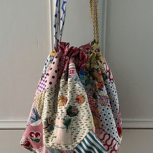 May include: A colorful patchwork drawstring bag with a yellow, blue, and white patterned strap. The bag is made of various fabrics with floral, geometric, and polka dot patterns. The text "Warnamboool Bag" is at the top of the image and the text "Margaret Sampson George" and "Take an Element" are at the bottom of the image.