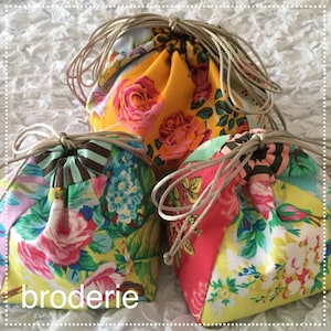 May include: Three colorful fabric drawstring bags with floral patterns. The bags are made of patchwork fabric and have a vintage aesthetic. The bags are tied with a brown cord.