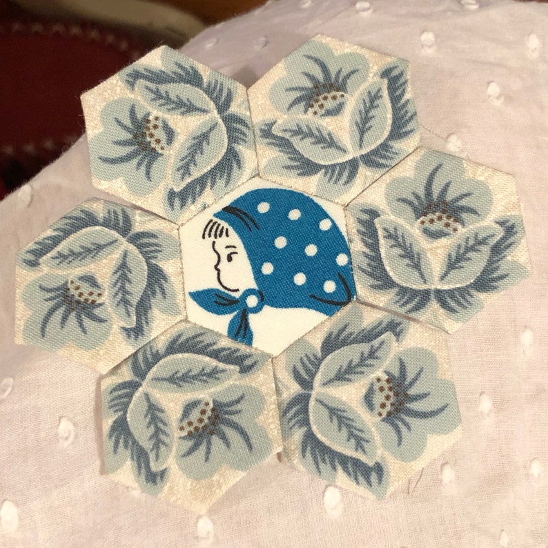May include: A blue and white fabric hexagon with a floral pattern. The center hexagon features a girl wearing a blue and white polka dot hat.