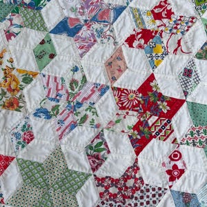 May include: Close-up of a handmade quilt with a star pattern. The quilt features a patchwork design with white fabric and various floral and geometric patterned fabrics in red, green, blue, and yellow. The quilt is likely made of cotton.
