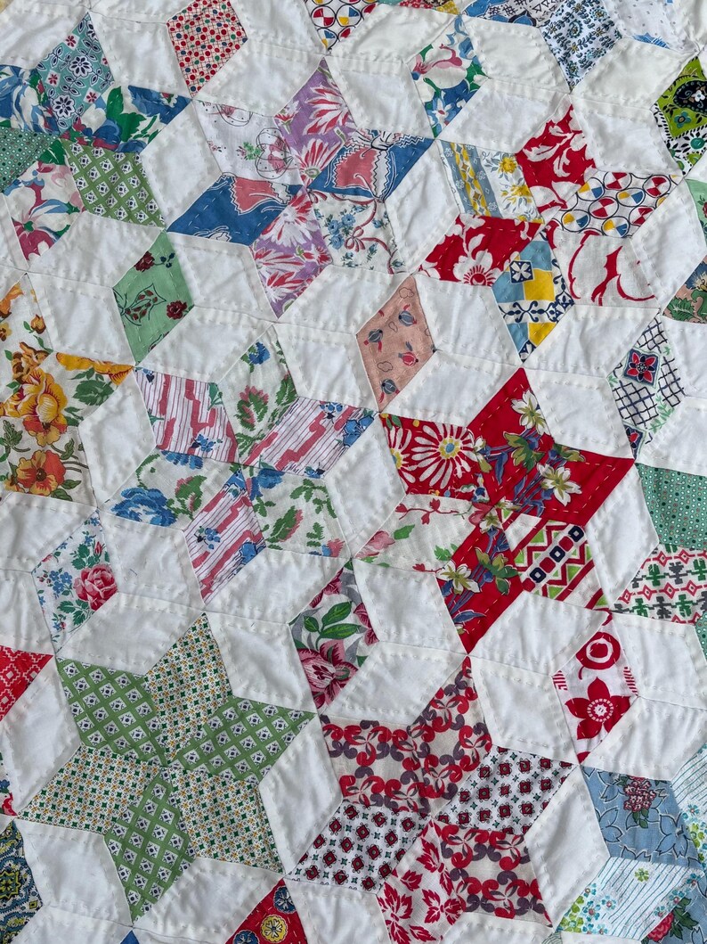 May include: Close-up of a handmade quilt with a star pattern. The quilt features a patchwork design with white fabric and various floral and geometric patterned fabrics in red, green, blue, and yellow. The quilt is likely made of cotton.