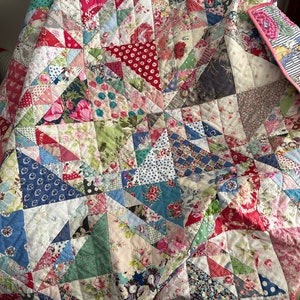 Peut inclure: Une courtepointe en patchwork composée de différents tissus floraux et à motifs dans des tons de rouge, bleu, vert et blanc. La courtepointe est composée de triangles et de carrés, créant un motif géométrique.