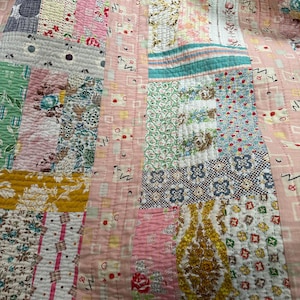 Puede incluir: Una colcha de retazos hecha con diferentes telas con estampados florales en tonos rosa, verde, azul y amarillo. La colcha est&aacute; cosida con hilo blanco y tiene una textura acolchada.