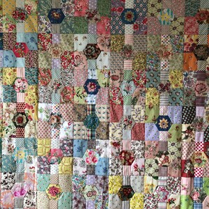 Puede incluir: Una colcha hecha de muchos cuadrados de tela diferentes, cada uno con un patr&oacute;n floral. La colcha est&aacute; hecha en estilo patchwork, con los cuadrados dispuestos en un patr&oacute;n aleatorio. La colcha est&aacute; en tonos de rosa, azul, verde, amarillo y marr&oacute;n.