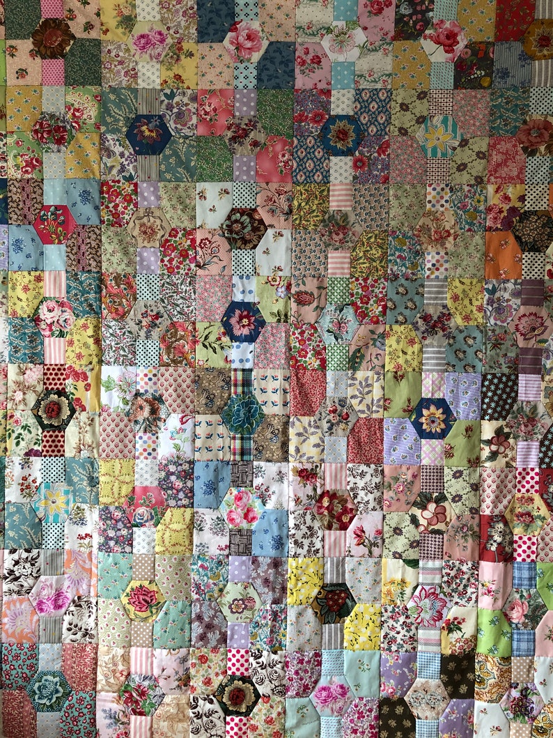 Puede incluir: Una colcha hecha de muchos cuadrados de tela diferentes, cada uno con un patr&oacute;n floral. La colcha est&aacute; hecha en estilo patchwork, con los cuadrados dispuestos en un patr&oacute;n aleatorio. La colcha est&aacute; en tonos de rosa, azul, verde, amarillo y marr&oacute;n.