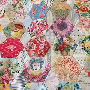 Puede incluir: Una colcha de retazos hecha de recortes de tela coloridos. La colcha está hecha de formas hexagonales, cada una con un patrón floral diferente. La colcha es una mezcla de colores brillantes, incluyendo rojo, rosa, azul, amarillo y verde.