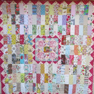 May include: A patchwork quilt featuring a pink and white floral design. The quilt is composed of numerous squares of fabric, each with a distinct pattern. The quilt is edged with a pink border containing white polka dots.