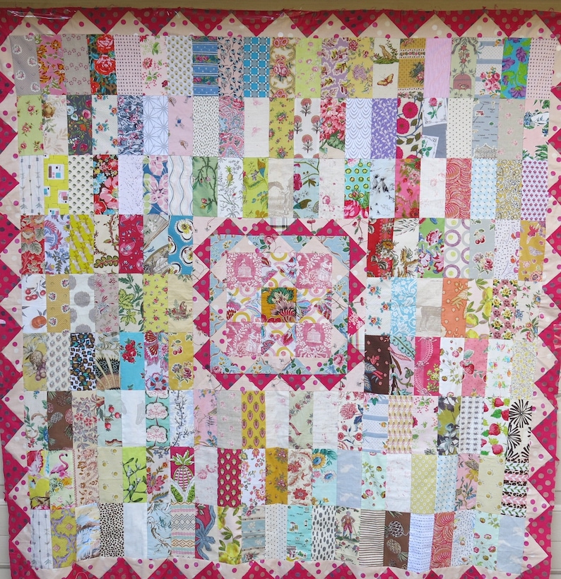 May include: A patchwork quilt with a pink and white floral pattern. The quilt is made up of many different squares of fabric, each with a unique design. The quilt is surrounded by a pink border with white polka dots.