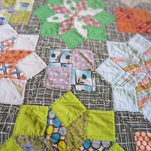 K&ouml;nnte beinhalten: Ein Patchwork-Deckenst&uuml;ck mit einer Vielzahl von bunten Stoffen und Mustern. Die Decke besteht aus Quadraten und Dreiecken, und die Farben umfassen Rot, Orange, Gelb, Gr&uuml;n, Blau und Lila.