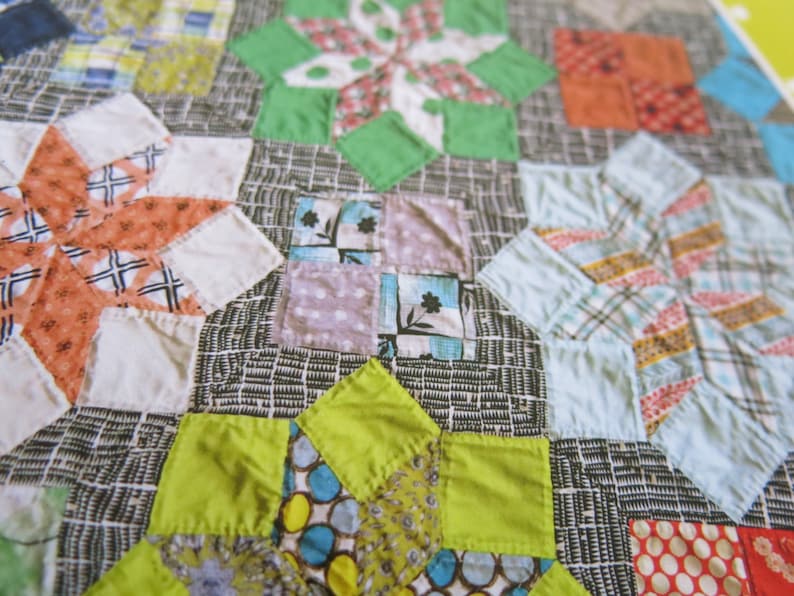 K&ouml;nnte beinhalten: Ein Patchwork-Deckenst&uuml;ck mit einer Vielzahl von bunten Stoffen und Mustern. Die Decke besteht aus Quadraten und Dreiecken, und die Farben umfassen Rot, Orange, Gelb, Gr&uuml;n, Blau und Lila.