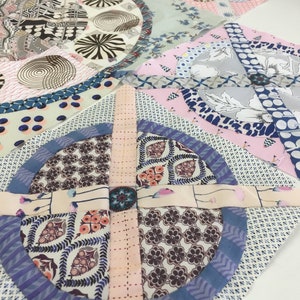 May include: A patchwork quilt block with a circular design in the center. The block is made of various fabrics with floral and geometric patterns in shades of pink, blue, and brown.