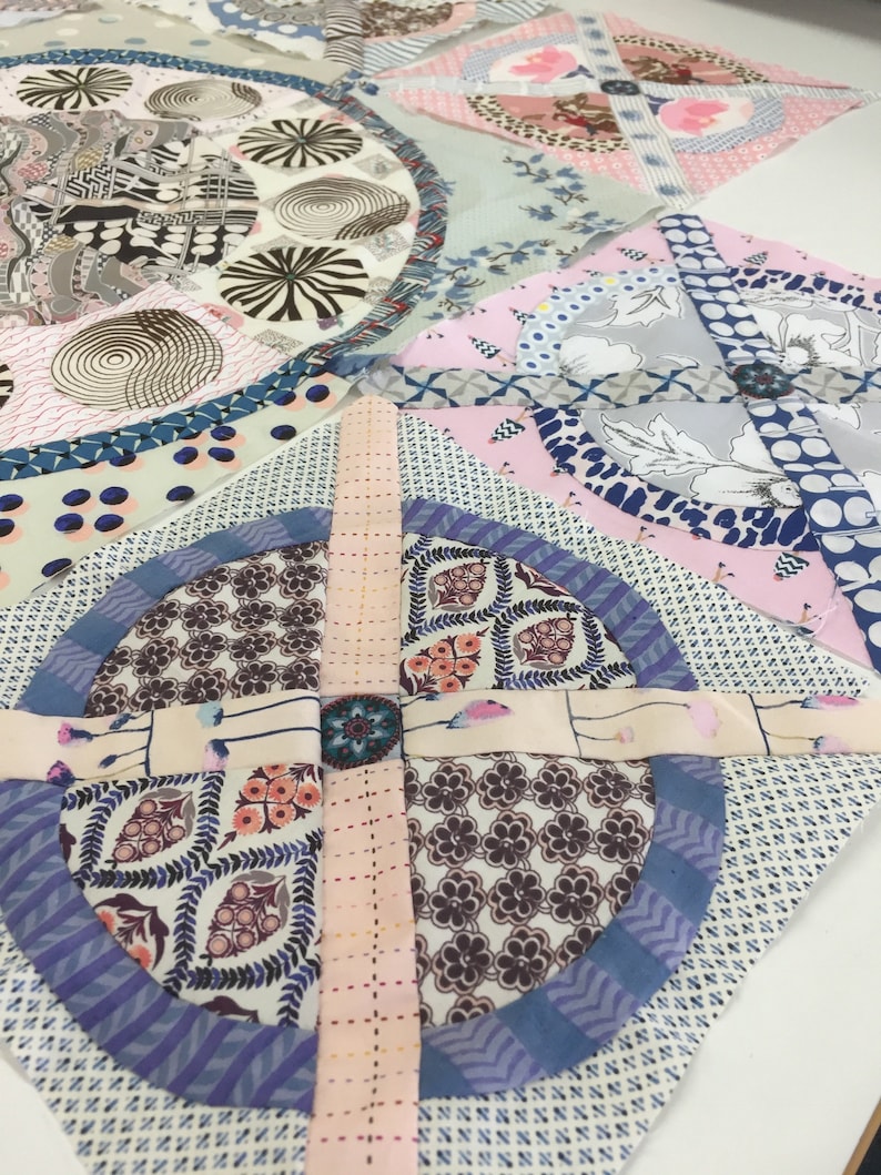 May include: A patchwork quilt block with a circular design in the center. The block is made of various fabrics with floral and geometric patterns in shades of pink, blue, and brown.