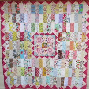 May include: A patchwork quilt with a pink and white floral pattern. The quilt is made up of many different fabrics, each with its own unique design. The quilt is bordered with a pink and white polka dot fabric.
