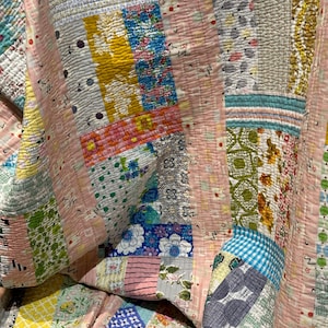 Puede incluir: Una colcha de retazos con una variedad de patrones florales y geom&eacute;tricos en tonos de rosa, azul, verde y amarillo. La colcha est&aacute; hecha de diferentes telas y texturas, creando un dise&ntilde;o &uacute;nico y colorido.