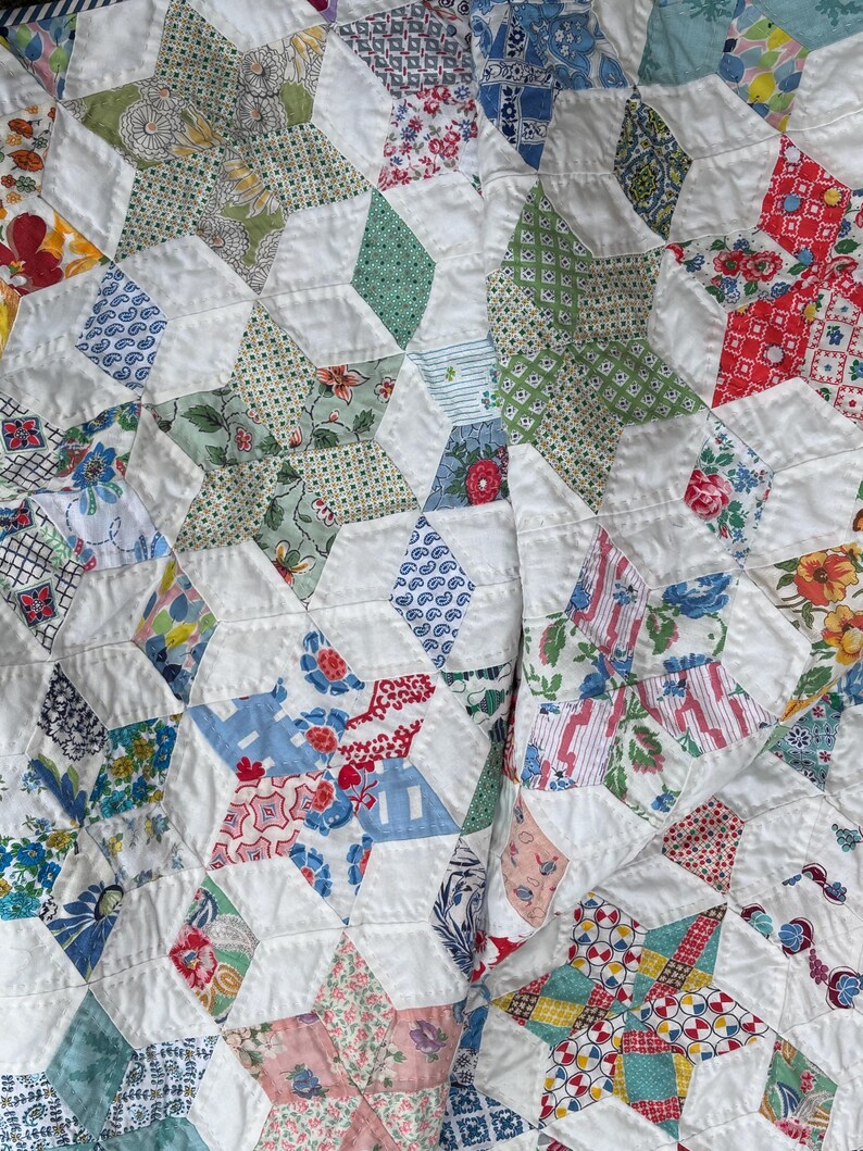 May include: Close-up of a handmade quilt featuring a star pattern. The quilt is composed of various fabric scraps in floral, geometric, and solid patterns. The stars are set against a white background.