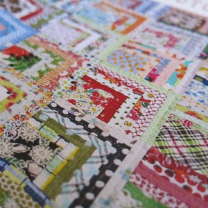May include: A patchwork quilt with a variety of colorful fabrics, including red, green, blue, and white. The quilt is made up of squares and rectangles, and the fabric is sewn together in a random pattern.