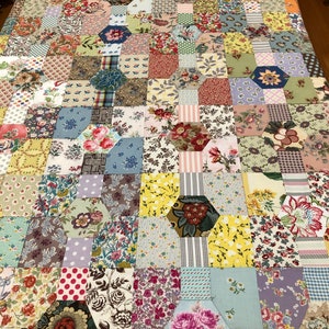 K&ouml;nnte beinhalten: Eine Decke aus bunten Stoffquadraten und -sechsecken. Die Decke zeigt eine Vielzahl von Blumenmustern und Farben, darunter Rosa, Blau, Gr&uuml;n, Gelb und Rot. Die Decke ist im Patchwork-Stil gefertigt und hat ein handgen&auml;htes Aussehen.
