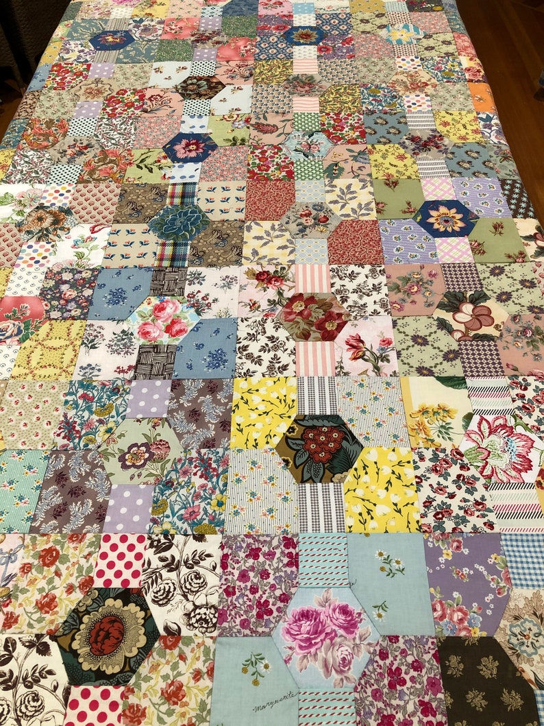 K&ouml;nnte beinhalten: Eine Decke aus bunten Stoffquadraten und -sechsecken. Die Decke zeigt eine Vielzahl von Blumenmustern und Farben, darunter Rosa, Blau, Gr&uuml;n, Gelb und Rot. Die Decke ist im Patchwork-Stil gefertigt und hat ein handgen&auml;htes Aussehen.