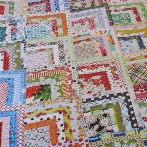 May include: A colorful quilt made with a patchwork of fabric squares. The squares are arranged in a pattern of overlapping squares, creating a layered effect. The quilt is made with a variety of fabrics, including floral prints, geometric patterns, and solid colors.