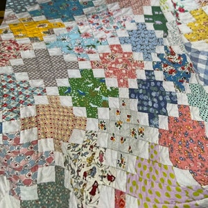 May include: A patchwork quilt with a variety of colorful floral and geometric patterns. The quilt is made up of squares and is sewn together in a cross-stitch pattern.