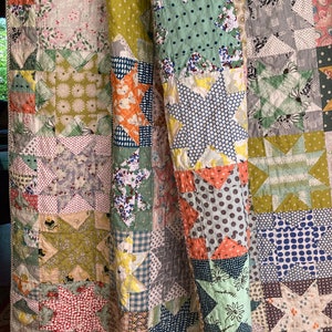Könnte beinhalten: Eine Patchwork-Decke mit einem Sternenmuster in Grün-, Blau-, Gelb- und Rosatönen. Die Decke besteht aus verschiedenen Stoffen mit unterschiedlichen Mustern, darunter Punkte, Blumenmuster und Gingham.