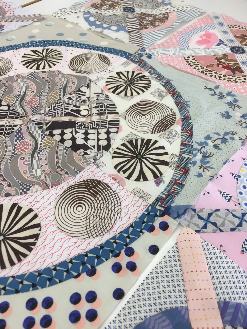 May include: A close-up of a quilt with a variety of colorful fabrics and patterns. The quilt features a circular design with a blue border and a white center. The center of the quilt is filled with a variety of geometric shapes and patterns, including circles, squares, and triangles. The quilt is made up of a variety of fabrics, including cotton, silk, and velvet.