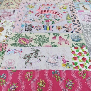 May include: A patchwork quilt with a variety of floral and animal patterns. The quilt is made up of different fabrics, including pink, green, and white. The quilt is stitched together with a white thread.