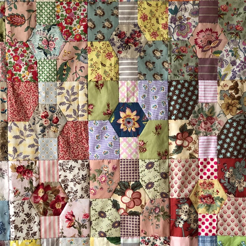 K&ouml;nnte beinhalten: Eine Patchwork-Decke mit einem sechseckigen Muster. Die Decke besteht aus verschiedenen Stoffen in den Farben Rosa, Gr&uuml;n, Blau, Braun und Wei&szlig;. Die Decke besteht aus vielen verschiedenen Blumenmustern.