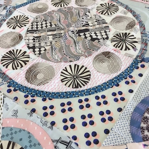 May include: A close-up of a quilt made of various fabrics with different patterns. The quilt features a central circle with a repeating pattern of black and white circles, surrounded by a ring of smaller circles with different patterns. The quilt is made of a variety of fabrics, including cotton, linen, and silk.