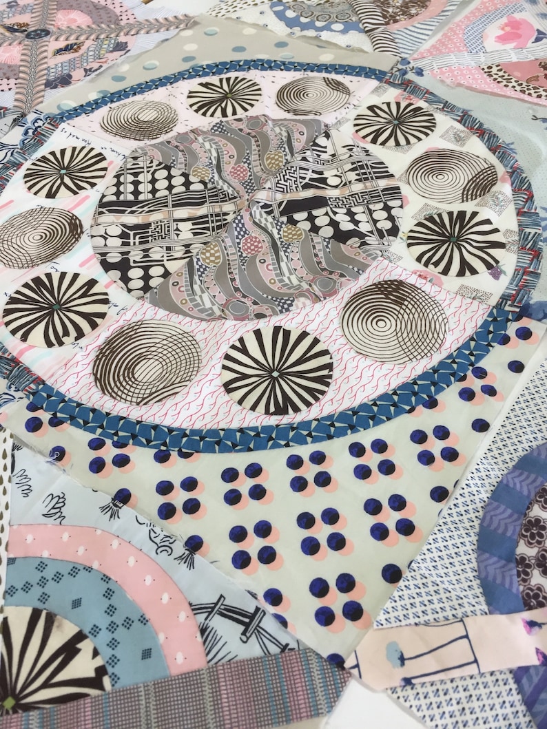 May include: A close-up of a quilt made of various fabrics with different patterns. The quilt features a central circle with a repeating pattern of black and white circles, surrounded by a ring of smaller circles with different patterns. The quilt is made of a variety of fabrics, including cotton, linen, and silk.