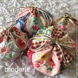 Puede incluir: Cuatro bolsas de tela con cordón de ajuste con diferentes patrones florales y a cuadros. Las bolsas están atadas con un cordón blanco y están sobre una superficie blanca texturizada. La palabra "broderie" está escrita en negro en la parte inferior de la imagen.